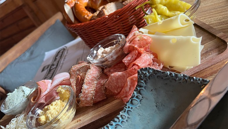 Eine rustikale Jause mit Wurst, Käse, Brot und Aufstrichen auf einem Holzteller.