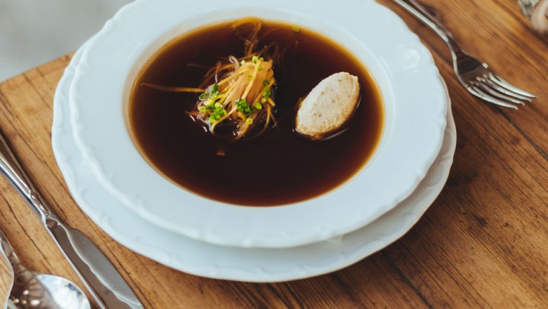 Eine klare Rindssuppe mit Gemüse und Knödel in einem weißen Teller auf einem Holztisch.