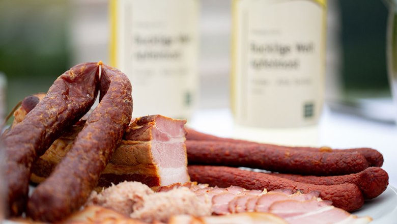 Nahaufnahme von Wurst- und Fleischspezialitäten auf einem Teller mit Flaschen im Hintergrund.