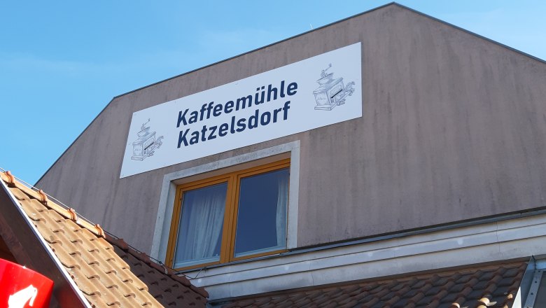 Geb&auml;ude mit Schild 'Kaffeem&uuml;hle Katzelsdorf' und Zeichnung einer Kaffeem&uuml;hle.