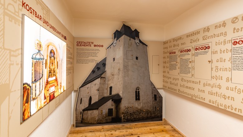 Innenansicht einer Ausstellung &uuml;ber Wehrkirchen mit Texttafeln und einem raumhohen Bild einer Kirche.