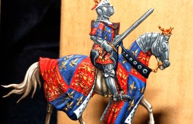 Zinnfigur eines Ritters in R&uuml;stung auf einem Pferd mit buntem Wappenrock.