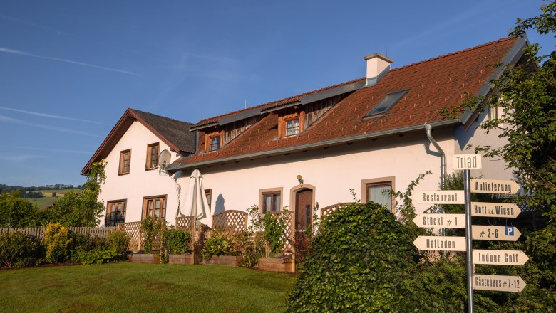 Ein weißes Gebäude mit rotem Dach und mehreren Schildern im Vordergrund, umgeben von grüner Landschaft.