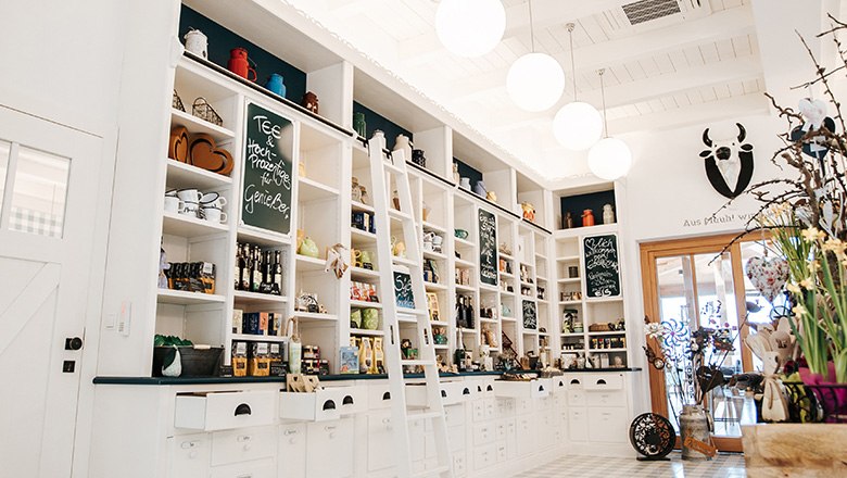 Hofladen mit weißen Regalwänden gefüllt mit diversen Produkten, daneben Dekoration.