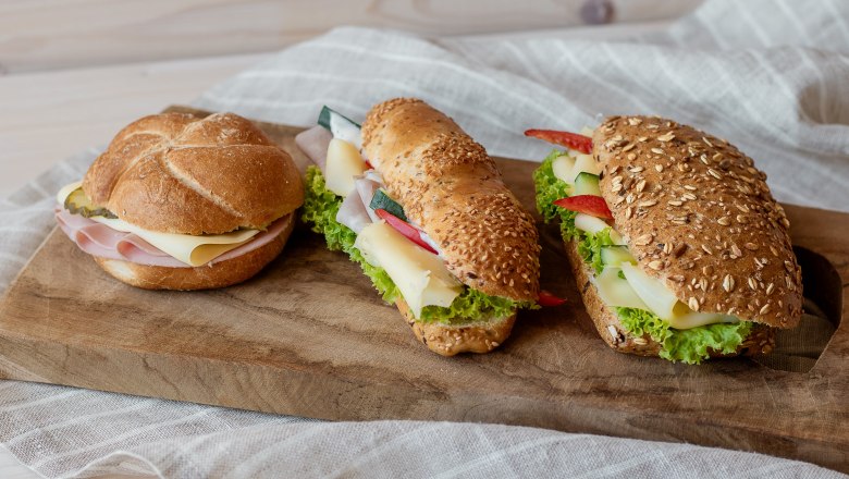 Drei belegte Brötchen auf einem Holzbrett.
