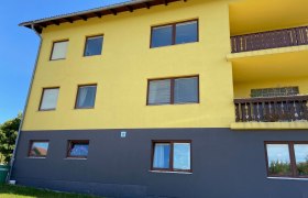 Gelbes Geb&auml;ude mit braunen Fenstern und Balkonen, blauer Himmel im Hintergrund.