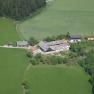 Luftaufnahme eines Bauernhofs inmitten von grünen Feldern und Wäldern.