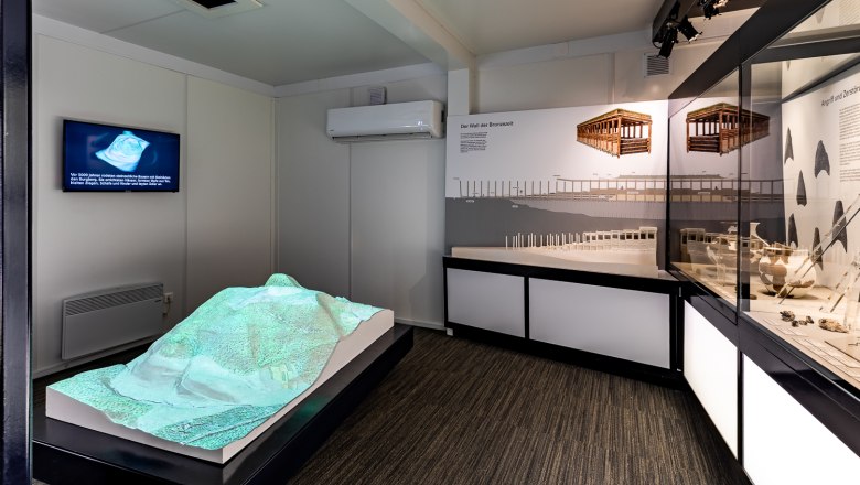 Innenansicht einer Ausstellung im Keltendorf Schwarzenbach mit Modellen und Informationstafeln.