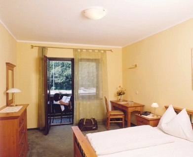 Ein gem&uuml;tliches Hotelzimmer mit Doppelbett, Schreibtisch, Kommode und Balkon mit Blick ins Gr&uuml;ne.