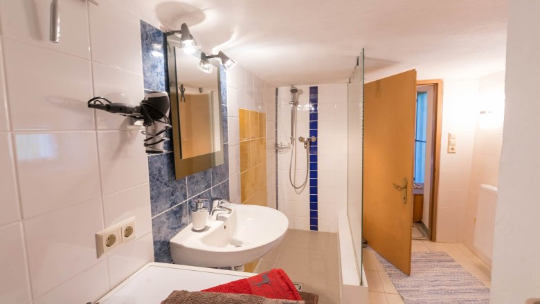 Ein Badezimmer mit Waschbecken, Spiegel, Dusche und Handt&uuml;chern.