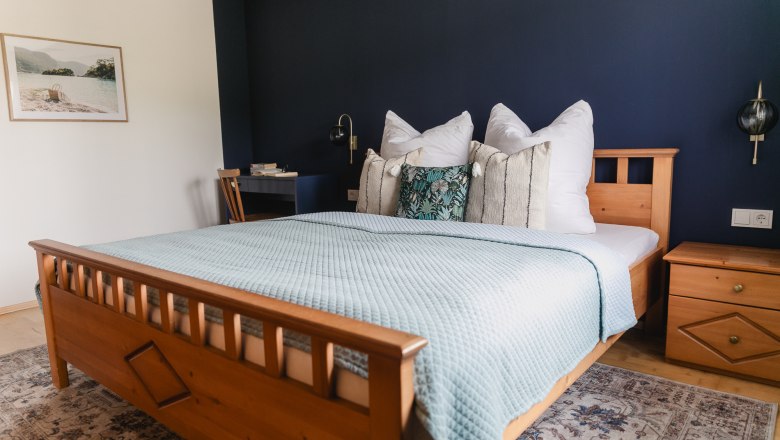 Gem&uuml;tliches Schlafzimmer mit Holzbett, blauer Wand und dekorativen Kissen.