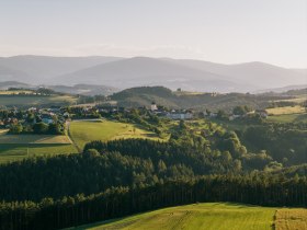 Landschaftsansicht von Lichtenegg in Pesendorf mit gr&uuml;nen Feldern und W&auml;ldern im Vordergrund und Bergen im Hintergrund.