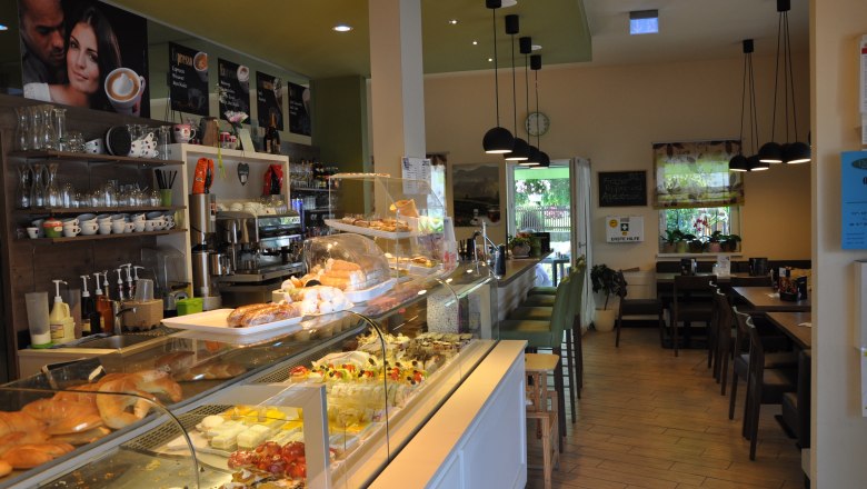 Innenansicht eines Cafés mit Theke voller Gebäck und Sitzbereich.