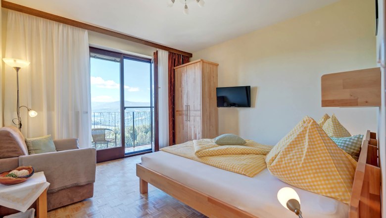 Helles Schlafzimmer mit Bett, Sofa, Schrank und Balkon mit Aussicht.