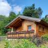 Holzhütte mit Blumen auf der Veranda in einer grünen Umgebung.