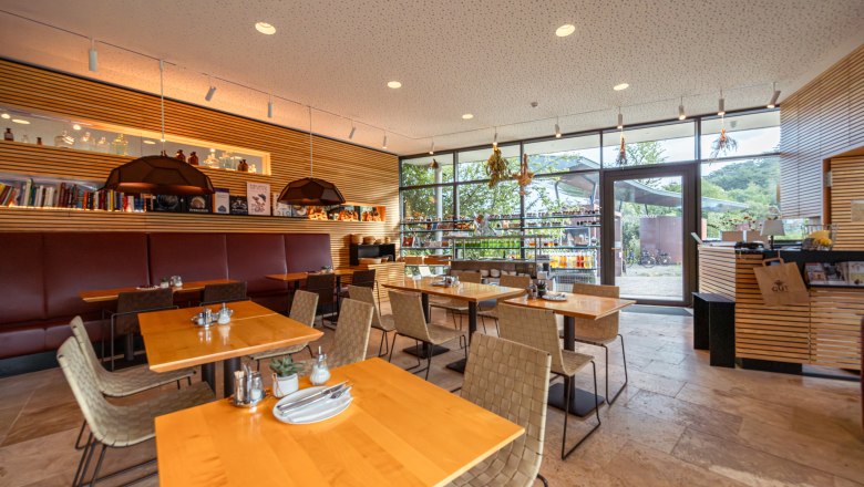 Innenansicht eines modernen Restaurants mit Holztischen und großen Fenstern.