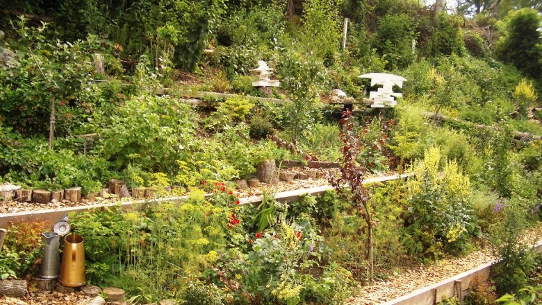 Terrassierter Garten mit &uuml;ppiger Vegetation und dekorativen Elementen.