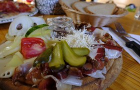 Ein Holzbrett mit Aufschnitt, K&auml;se, Gurken, Tomaten und Zwiebeln, daneben ein Brotkorb.