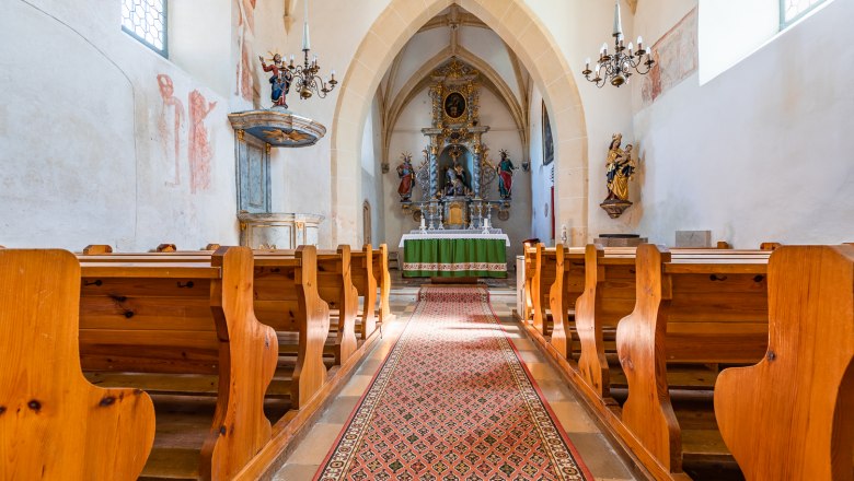 Innenansicht der Wehrkirche Bad Sch&ouml;nau mit Holzb&auml;nken, Altar und verzierten W&auml;nden.