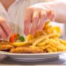 Ein Teller mit Wiener Schnitzel, Pommes frites, Zitrone und Tomate wird von einer Person angerichtet.