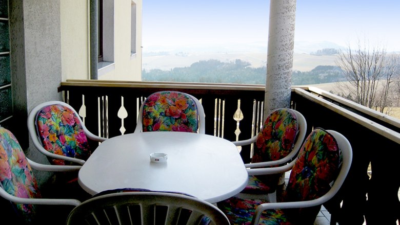 Balkon mit Tisch und bunten Stühlen, Aussicht auf Landschaft.