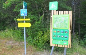 Wegweiser und Informationstafel für Radfahrer in Bad Erlach, umgeben von Bäumen.