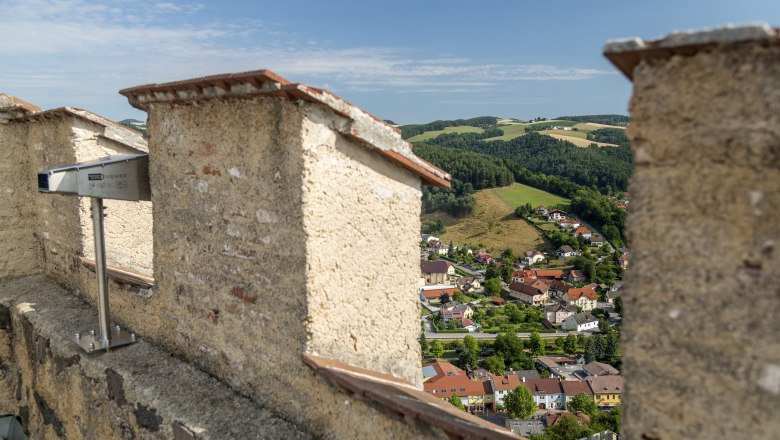 Aussicht von einer Burgruine auf eine Stadt und gr&uuml;ne H&uuml;gel.