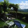 Gartenlaube mit Tisch und Bänken, umgeben von grüner Landschaft und zwei Liegestühlen im Vordergrund.