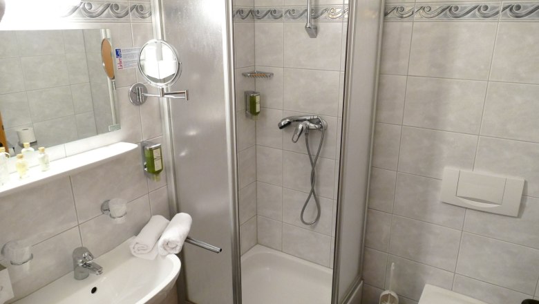 Badezimmer mit Dusche, Waschbecken und Spiegel.