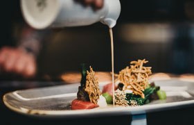 Soße wird über einen fein angerichteten Teller mit Essen gegossen