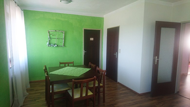 Essbereich mit grün gestrichener Wand, Holztisch und Stühlen.