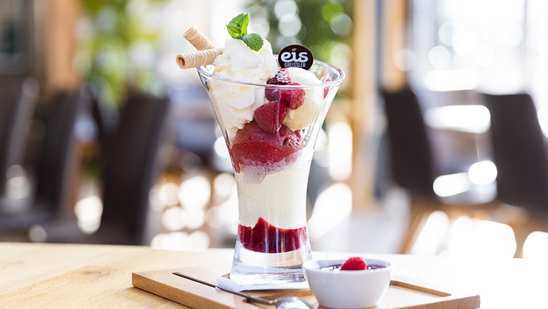 Ein Eisbecher mit Fruchteis, Schlagobers, Waffeln und Himbeeren auf einem Holzbrett., © Blochberger Eisproduktion GmbH