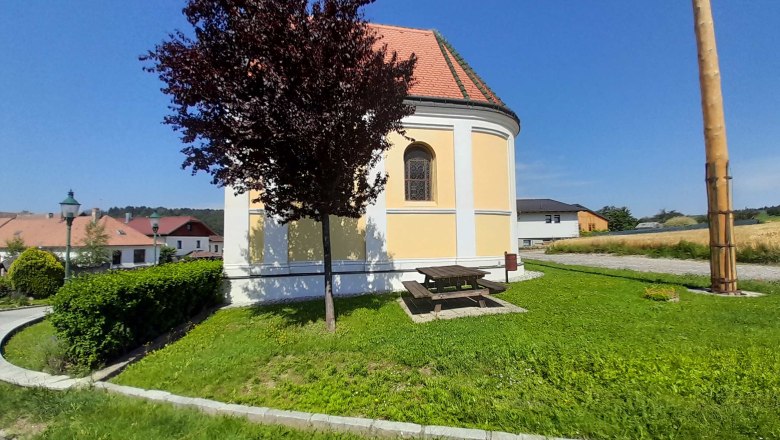 Runde Kirche mit gelber Fassade, umgeben von grüner Wiese und Bäumen, bei sonnigem Wetter.