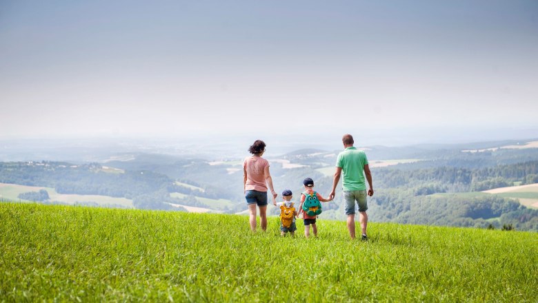 Familie spaziert &uuml;ber eine gr&uuml;ne Wiese mit weitem Blick auf die Landschaft.