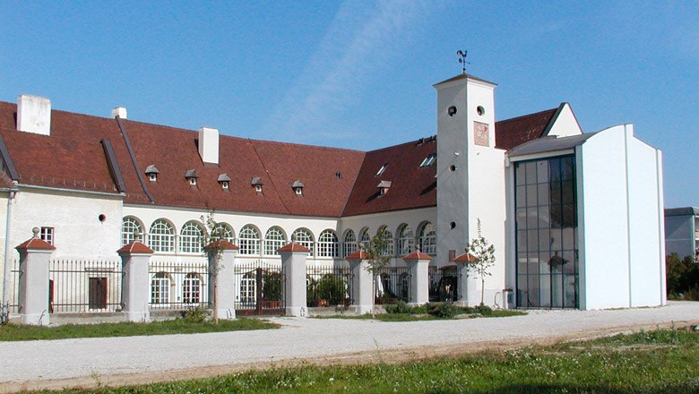Schloss Katzelsdorf mit modernem Anbau und historischem Gebäude. Weiße Fassade mit gerundeten Fenstern, rotes Dach und großer Innenhof