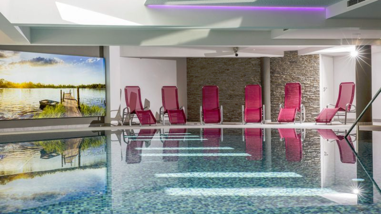 Hallenbad mit roten Liegestühlen, Steinwänden und einem großen Wandbild.