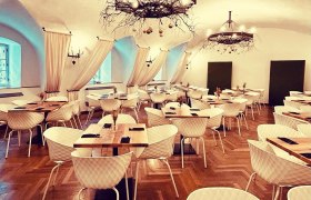 Eleganter Speisesaal mit Parkettboden, weißen Stühlen, Holztischen und dekorativen Kronleuchtern.