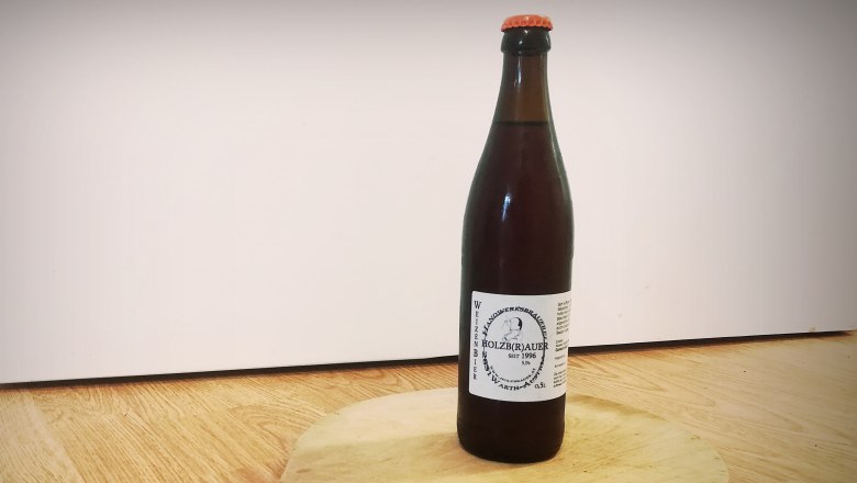 Eine Flasche Weizenbier vom Holzbr&auml;u steht auf einem runden Holzbrett mit Griff.