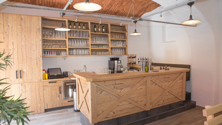 Schank aus Holz mit Gl&auml;sern und Flaschen und Backsteindecke.