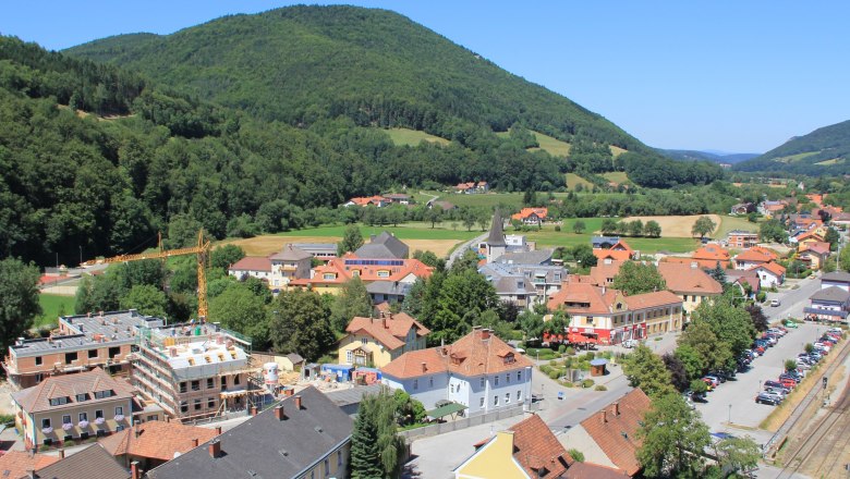 Luftaufnahme von Grimmenstein mit Häusern, Baukran und grünen Hügeln im Hintergrund.