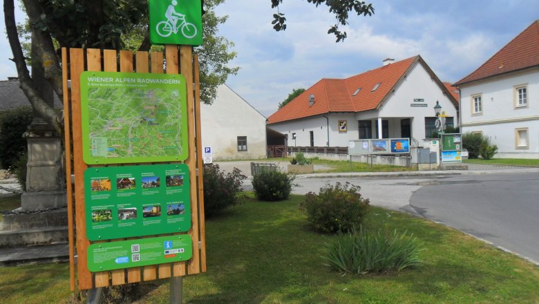 Radstartplatz-Tafel in Walpersbach mit Karte und Informationen, umgeben von Gebäuden und Bäumen.