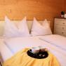 Gemütliches Schlafzimmer mit Doppelbett, weißen Kissen und Decken, gelber Decke, Tablett mit Tassen, Nachttischlampe und Kommode mit Handtüchern.