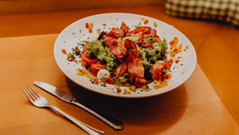 Ein Teller mit gemischtem Salat, Ziegenk&auml;se und Speck auf einem Holztisch.