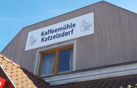 Geb&auml;ude mit Schild 'Kaffeem&uuml;hle Katzelsdorf' und Zeichnung einer Kaffeem&uuml;hle.