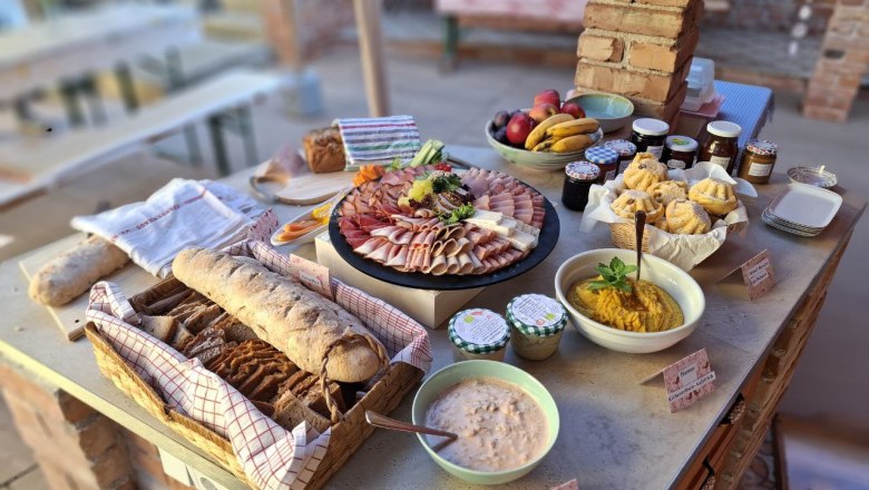 Ein Buffet mit Brot, Aufschnitt, Obst, Marmeladen und Dips auf einem Tisch.