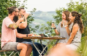 4 Leuten stoßen mit Most bei einem Heurigen an.