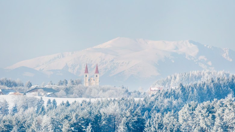 Winterlandschaft mit Kirche und Bergen im Hintergrund.