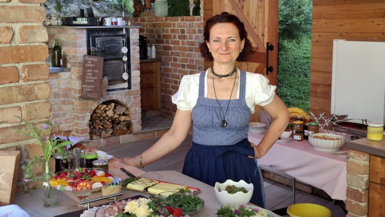 Die Chefin in traditioneller Kleidung in einer rustikalen Küche mit Speisen.
