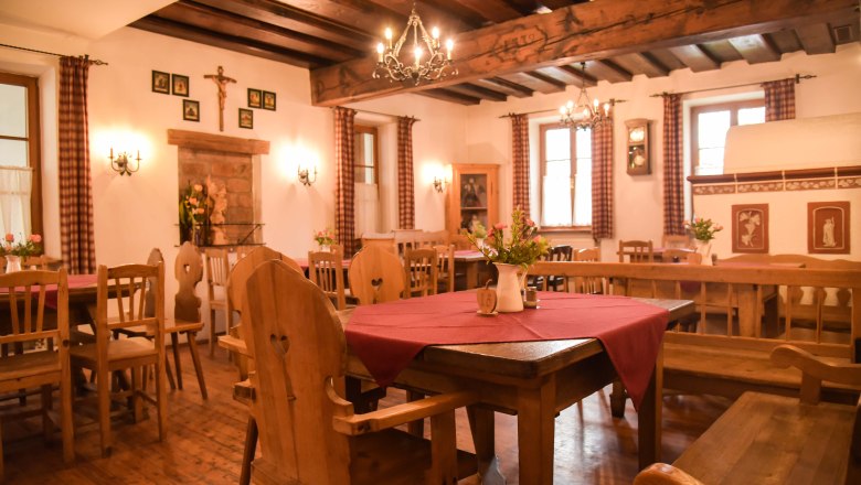 Gemütliche Stube mit Holzmöbeln, roten Tischdecken und Kronleuchtern.