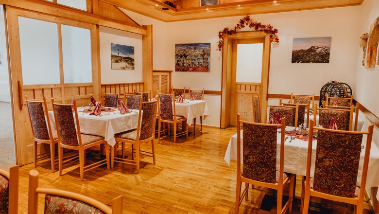 Gem&uuml;tliche Gaststube mit Holzm&ouml;beln und dekorierten Tischen, umgeben von Bildern an den W&auml;nden.